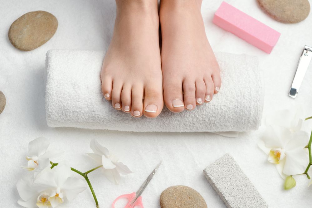 Gepflegte Füße mit hellem Nagellack auf einem weißen Handtuch, umgeben von Orchideen und Pflegeutensilien