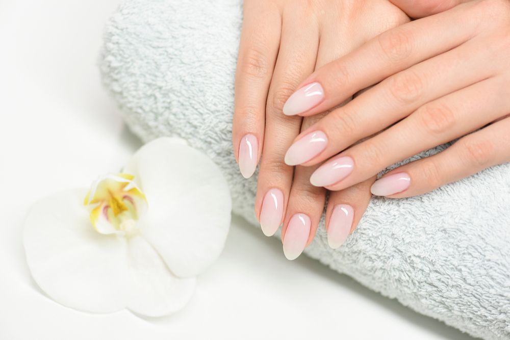 Gepflegte Hände mit natürlich lackierten Nägeln auf einem Handtuch neben einer weißen Orchidee