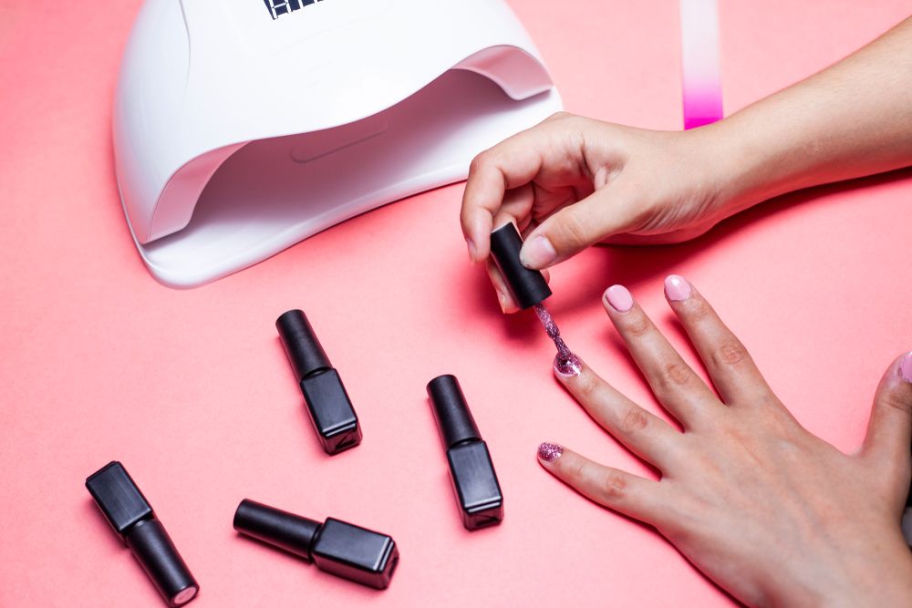 Fingernägel werden mit Gel-Lack in Rosé lackiert, daneben eine UV-Lampe und Lackfläschchen