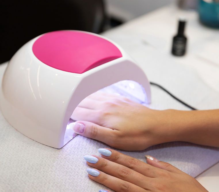 Frisch lackierte Shellac-Nägel in Hellblau werden unter einer UV-Lampe ausgehärtet